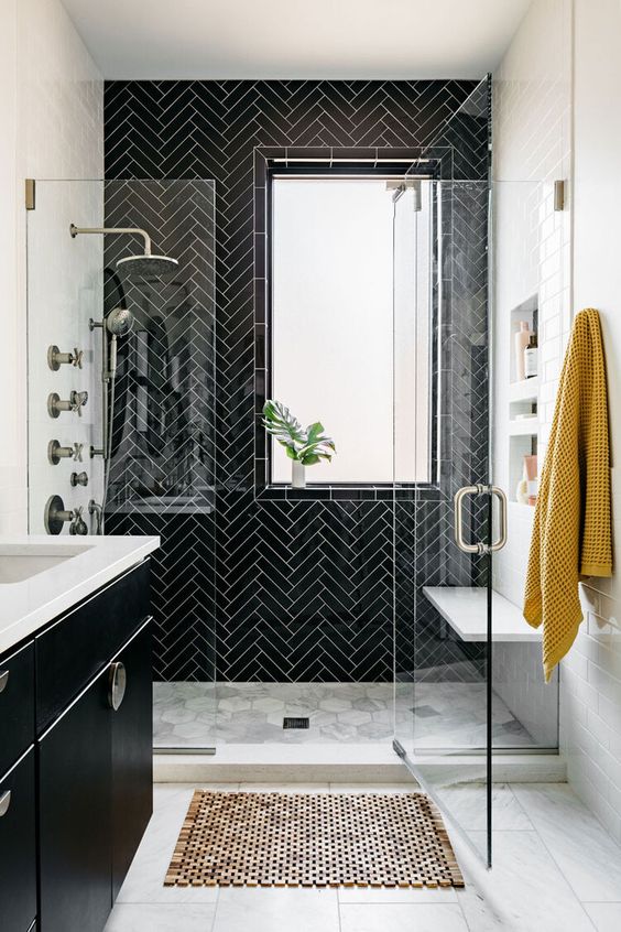 a black and white bathroom with herringbone tiles on the wall, a bench, niche shelves, a black vanity and a tiled floor