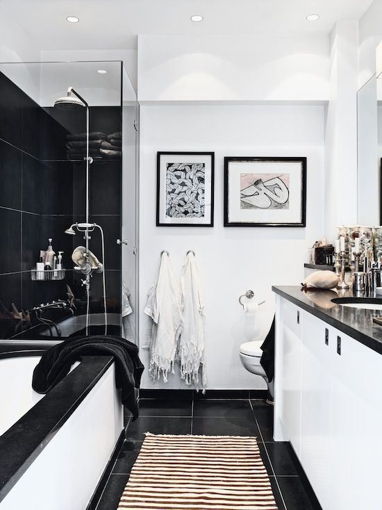 a black and white bathroom with large format tiles, a tub with black edge, a black shower space and a white vanity