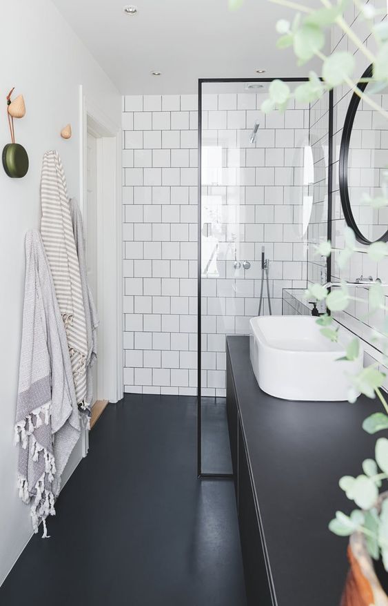 a black and white bathroom with square tiles, a black floor and a large black vanity plus a round mirror in a black frame