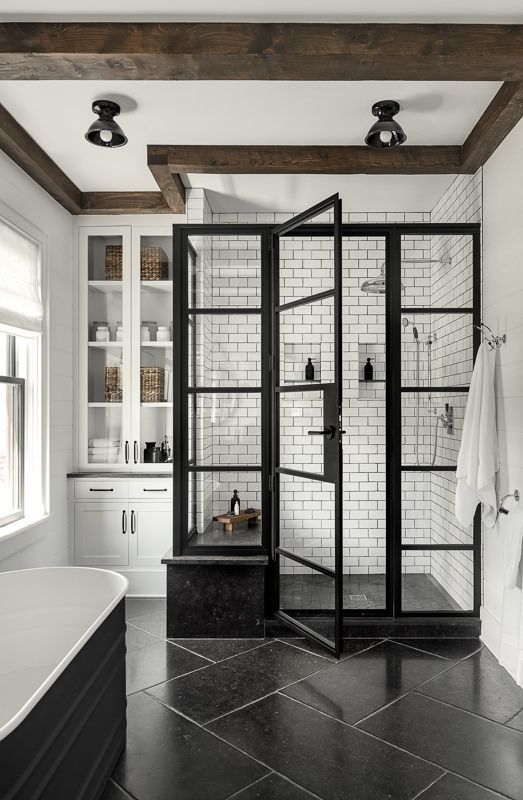 A black and white farmhouse bathroom with subway tiles and a black floor, a shower space, a built in storage unit and a black tub