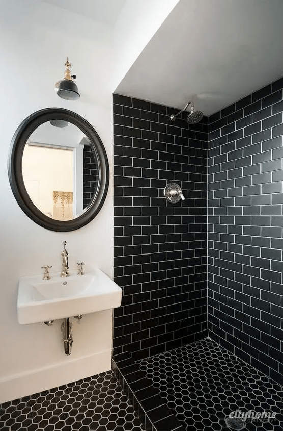 A bold bathroom with black subway tiles in the shower, black hex tiles on the floor, a mirror in a black frame and wall mounted sink