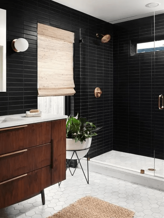 A mid century modern bathroom with black skinny and white hex tiles, a stained vanity, a shower space, brass fixtures and potted plants