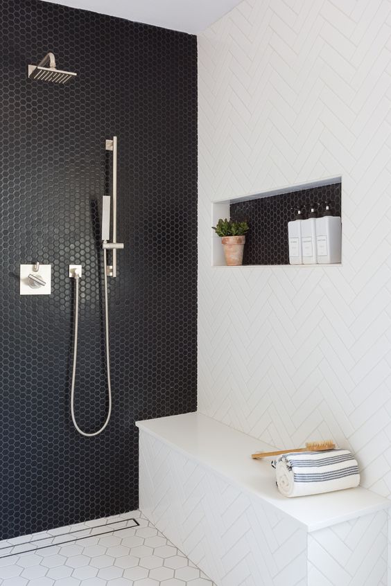 a modern black and white shower space with a penny tile wall and a herringbone one, a hex tile floor and a niche shelf
