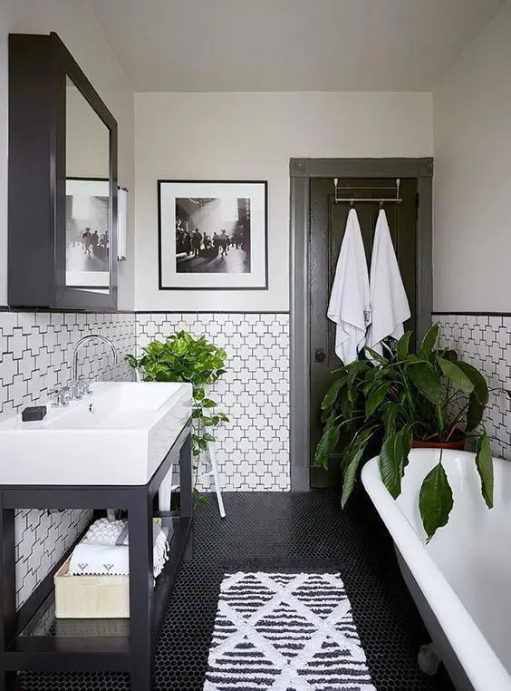 A pretty black and white bathroom with penny and eye catchy geometric tiles, a clawfoot tub, a sink on a black stand and a mirror cabinet