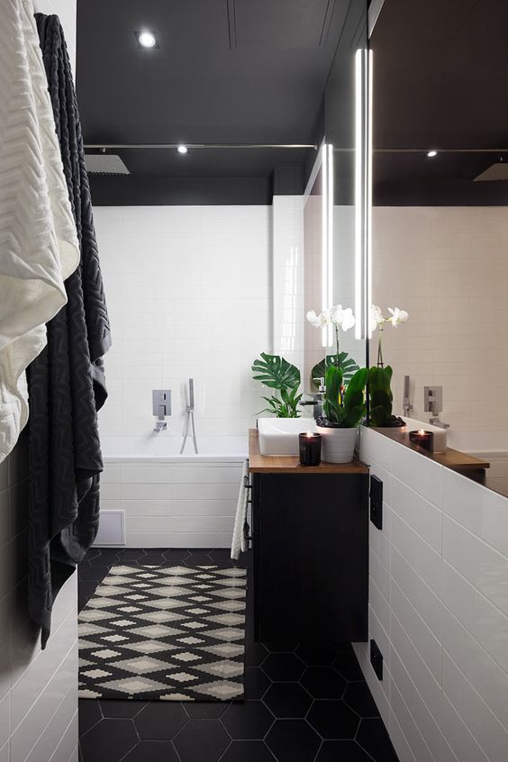 a pretty black and white bathroom with white tiles and a black ceiling, a black hex tile floor, a black vanity and a mirror