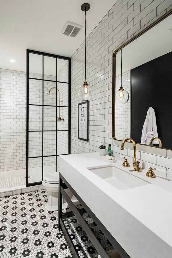 a refined black and white bathroom with subway and penny tiles, a stand with a sink, a large mirror and gold fixtures