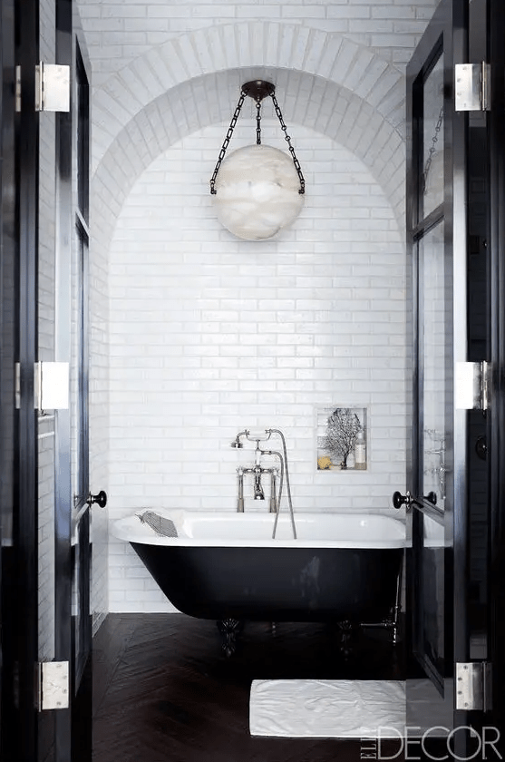 a retro black and white bathroom with white subway tiles, a black clawfoot tub, a pendant lamp and a niche for storage