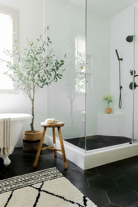 a serene bathroom with white tiles on the walls and black hex ones on the floor, a clawfoot tub and a shower space