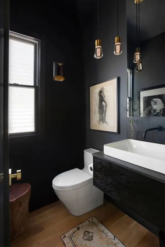 a small powder room with black walls, a black floating vanity, a mirror and pendant bulbs and a tree stump stool