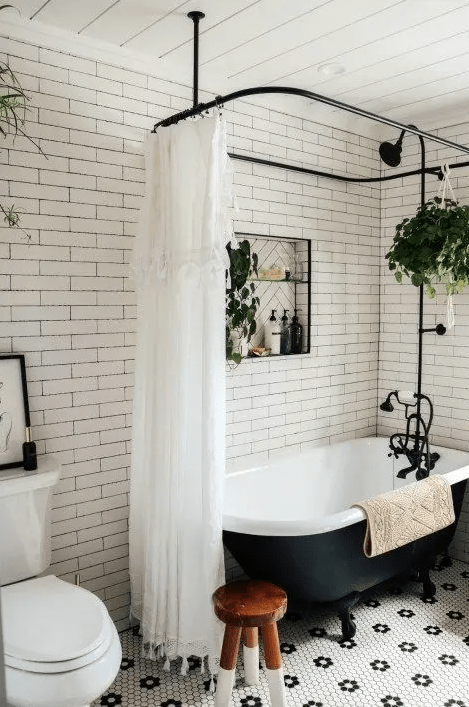 a small retro bathroom clad with white subway and penny tiles, a vintage black tub, black fixtures and potted plants is cool