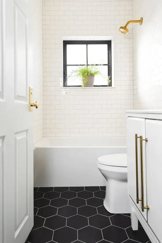 a small yet cool bathroom done with white subway tiles and black hex ones, gold touches and potted greenery is a lovely space