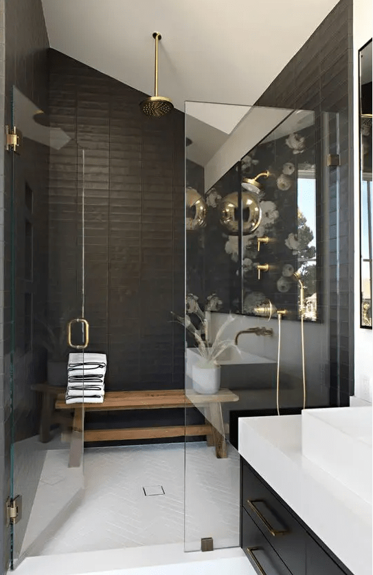 a stylish black and white bathroom with a shower space, a bench, gold fixtures, a black vanity and a white stone countertop