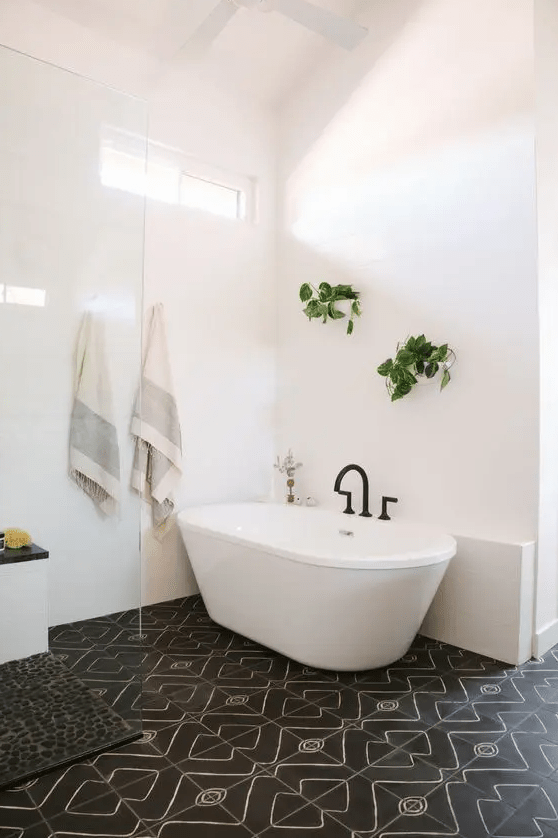a stylish mid-century modern bathroom with white and black mosaic tiles, a tub, greenery and a black pebble rug