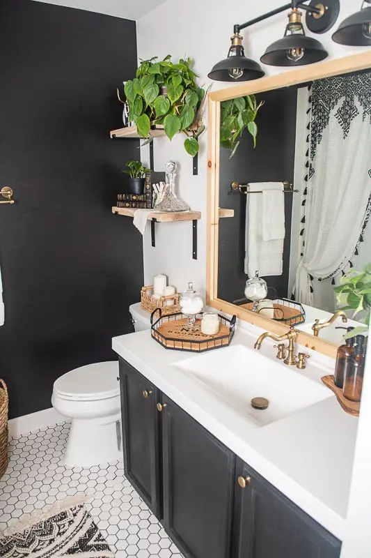 A vintage style bathroom with a black accent wall and a black vanity, white appliances, stained shelves and a mirror in a stained frame