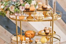 a chic Thanksgiving bar cart with a lush floral centerpiece, glass stands and bowls, candles and pumpkins