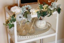 a chic bar cart with fake greenery and flower garland, faux pumpkins and a sign with lights