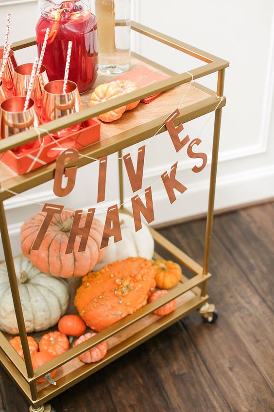 a chic brass bar cart with a letter banner, pumpkins on the lower level and copper mugs for drinks