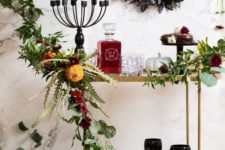 a dramatic bar cart with black glasses, a candelabra, a black butterfly wreath and a lush greenery garland