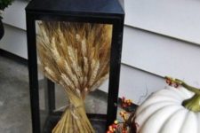 a lantern with wheat on display and little pumpkins around for a chic and timeless fall look