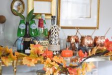 a refined bar cart with little fake pumpkins, a faux leaf garland and copper mugs