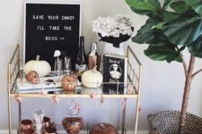 a stylish bar cart with copper touches, faux pumpkins, white blooms and a modern sign