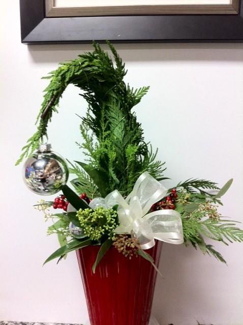 a Grinch Christmas tree in a red pot, with fresh greenery, a whte bow and a single silver ornament