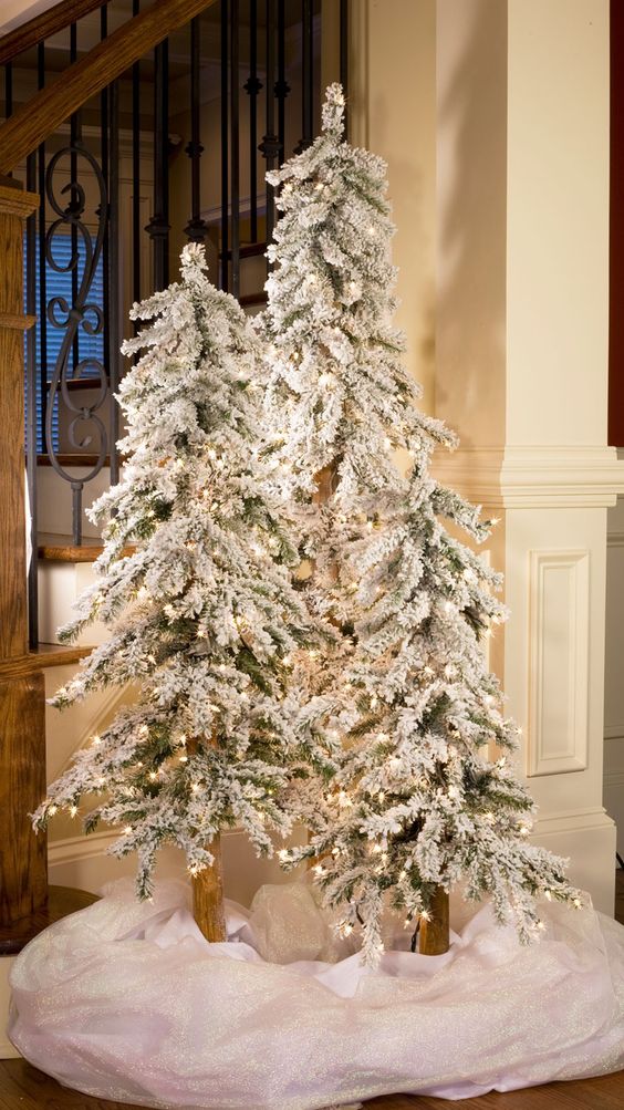 create a winter wonderland with a trio of flocked Christmas trees with lights and some white fabric at the base