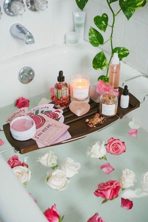 pink and white roses floating in the tub, a caddy with pink soap, candles, masks and moisturizers