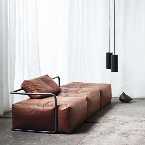 a minimalist brown leather sofa with black framing and black pendant lamps that echo