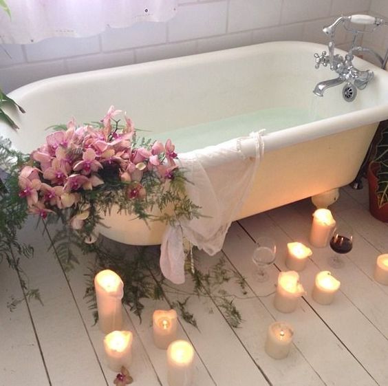 a bathtub decorated with pink blooms and ferns, candles on the floor and some wine