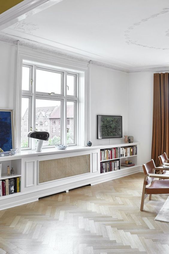 a Scandinavian dining room with a radiator covered with a screen, bookshelves, some art, a table lamp and amber leather chairs