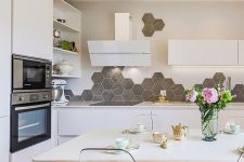 a Scandinavian eat-in kitchen with sleek white cabinets, a grey hexagon tile backsplash, built-in lights and a dining set