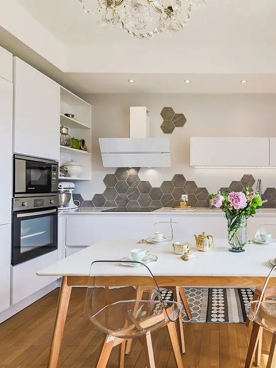 A Scandinavian eat in kitchen with sleek white cabinets, a grey hexagon tile backsplash, built in lights and a dining set