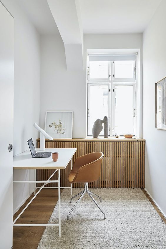 a Scandinavian home office with a radiator covered with a planked screen, a sleek desk and an amber leather chair, some decor