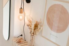 a Scandinavian space with a radiator covered with planks, with some dried leaves and herbs, a candle, a bulb hanging on the rook and an artwork