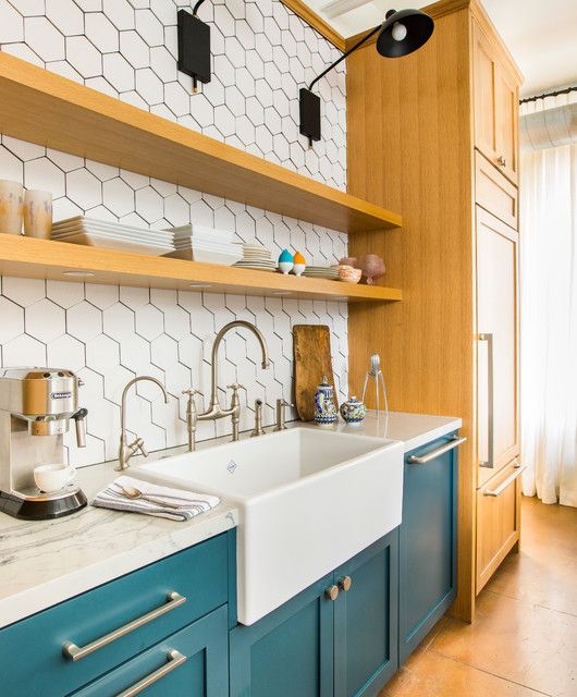a beautiful teal and stained kitchen with a white hexagon tile backsplash, white stone countertops and black sconces