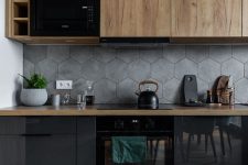a black and stained kitchen with butcherblock countertops, a grey hexagon tile backsplash and black appliances