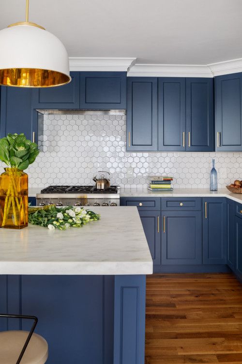 a bold blue kitchen with white stone countertops, a white hexagon tile backsplash, a white pendant lamp and greenery