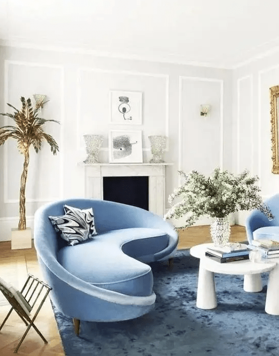 a charming living room with a curved blue sofa and matching chairs and a bold table that catch an eye