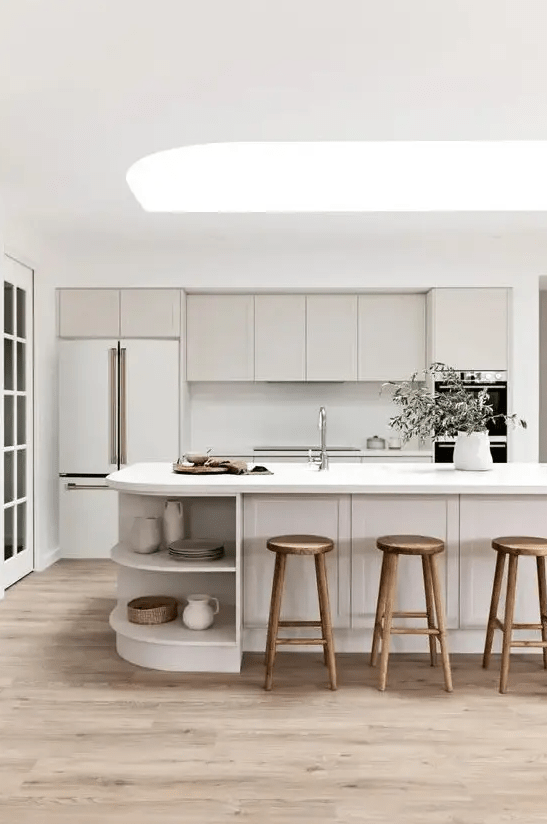 a chic neutral kitchen with shaker style cabinets, a curved kitchen island with open storage compartments and a skylight over it