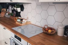 a classic white Scandinavian kitchen with usual and glass cabinets, butcherblock countertops and a black and white hex tile backsplash