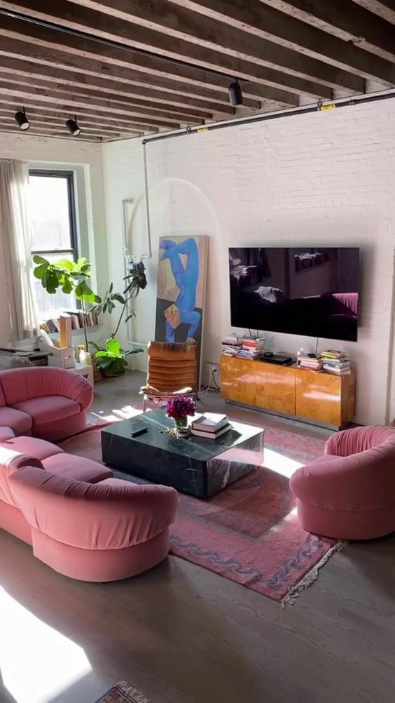 a colorful living room with pink curved seating furniture, a stone slab coffee table, a pink rug and a potted plant, some art