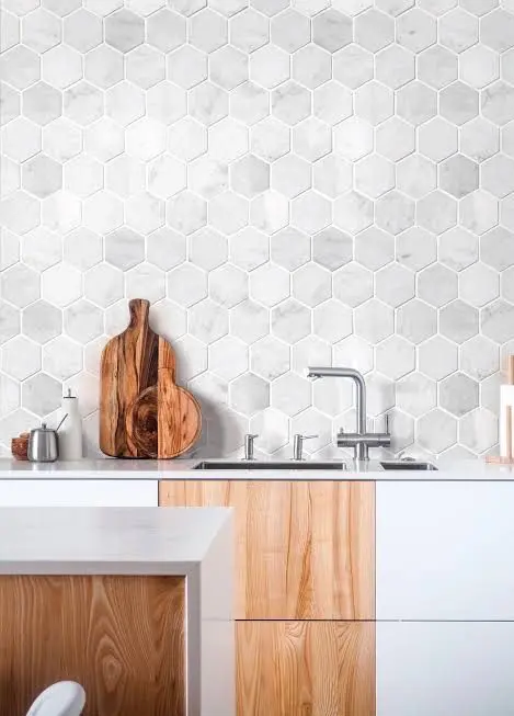 a contemporary kitchen with white and stained cabinets, a whole wall clad with grey marble hex tiles and white countertops