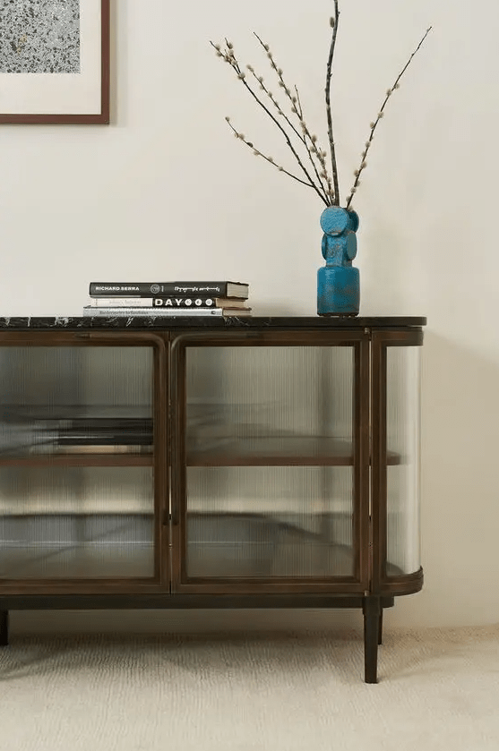 A curved credenza with reeded glass and dark framing, tall black legs and a black stone countertop is an elegant idea for a mid century modern space
