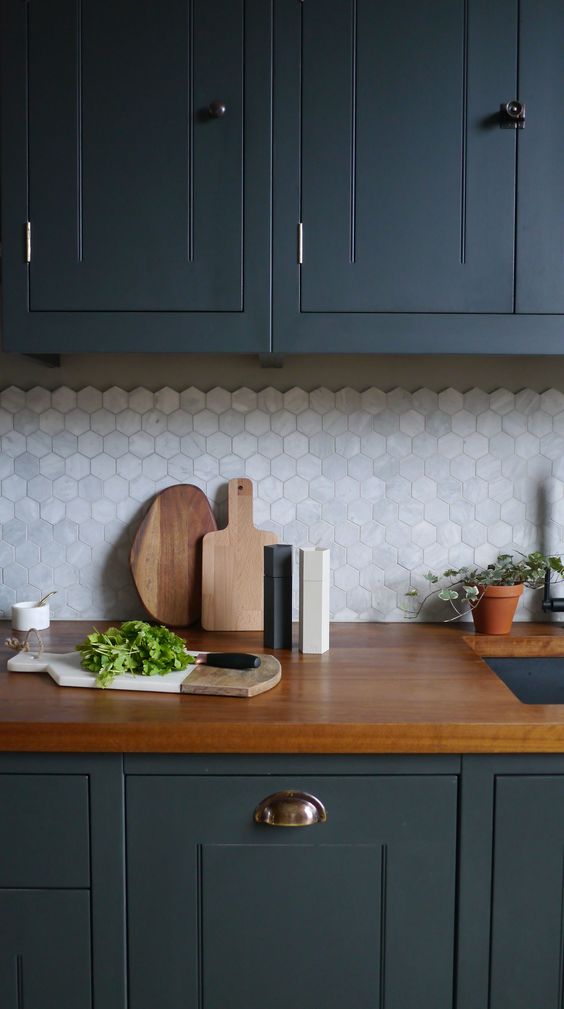 a dark grey kitchen with rich-stained countertops, a white marble hex tile backsplash and potted greenery and herbs