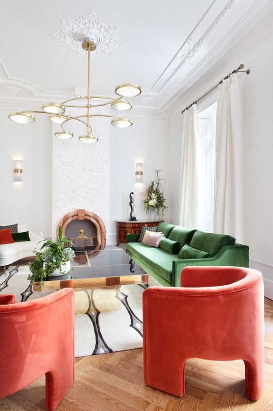 a fantastic living room with a glossy table, a green and white sofa, coral curved chairs, a lovely chandelier and some unique decor