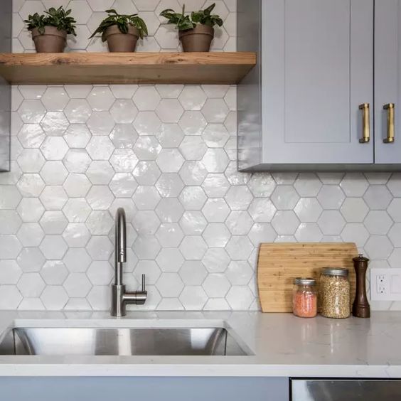 a grey kitchen with white stone countertops and a glossy white hexagon tile backsplash plus stained shelves