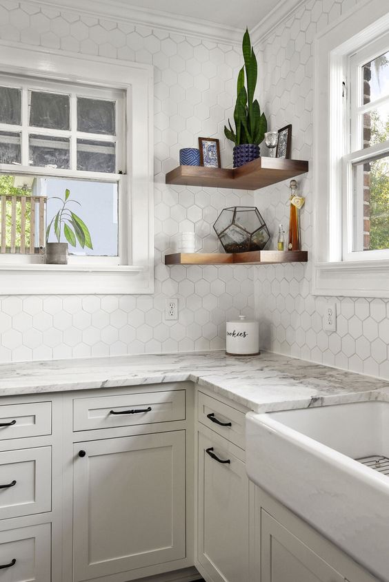 a lovely neutral kitchen with shaker cabinets, white stone countertops, a white hexagon tile backsplash, corner shelves