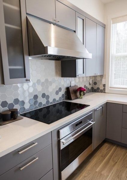 a modern grey kitchen with white stone countertops and an ombre hexagon tile backsplash plus stainless steel appliances