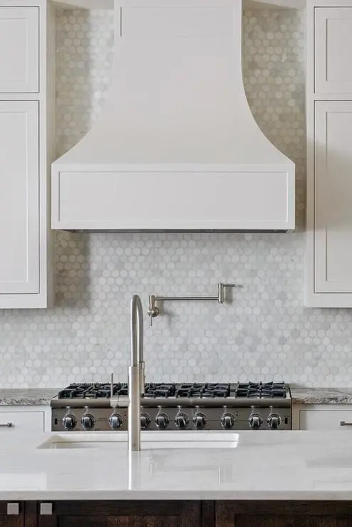 a neutral traditional kitchen with a stained kitchen island, a large hood and a marble hexagon tile backsplash